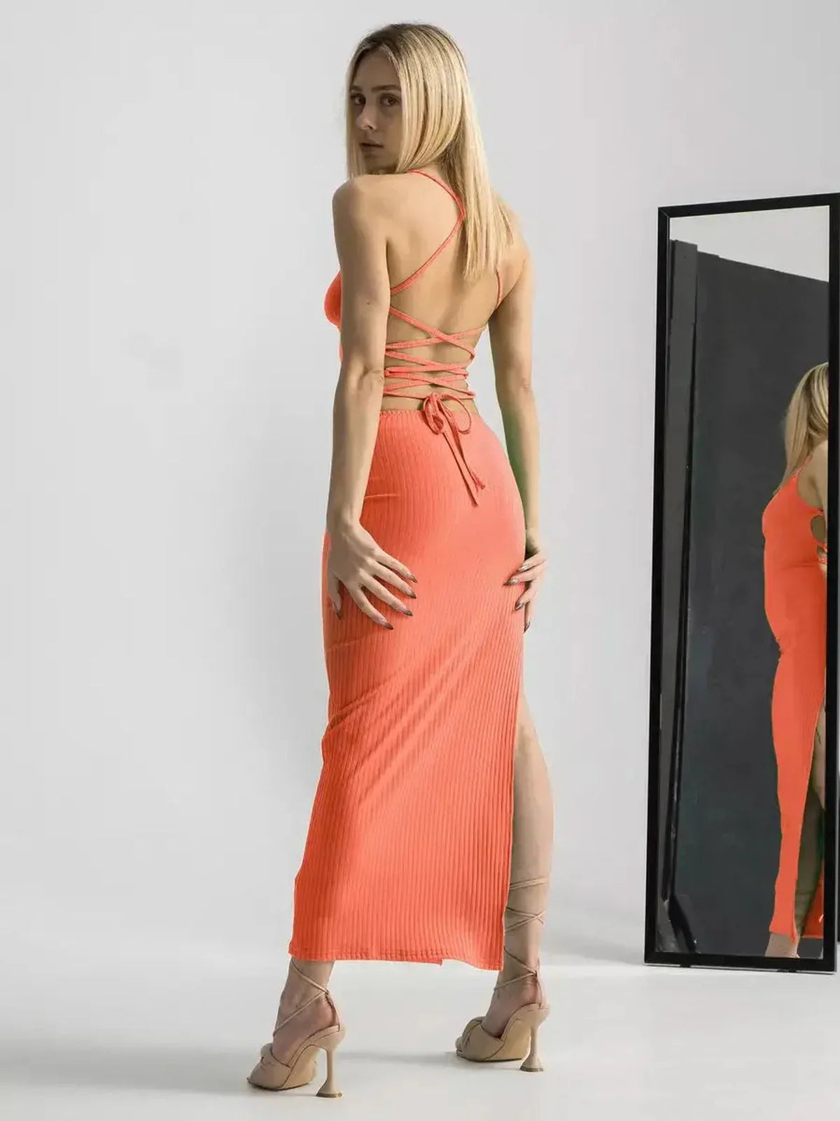Model showcasing the Maxi Dress Sunset Bloom with an open back and high slit in a stunning coral hue.