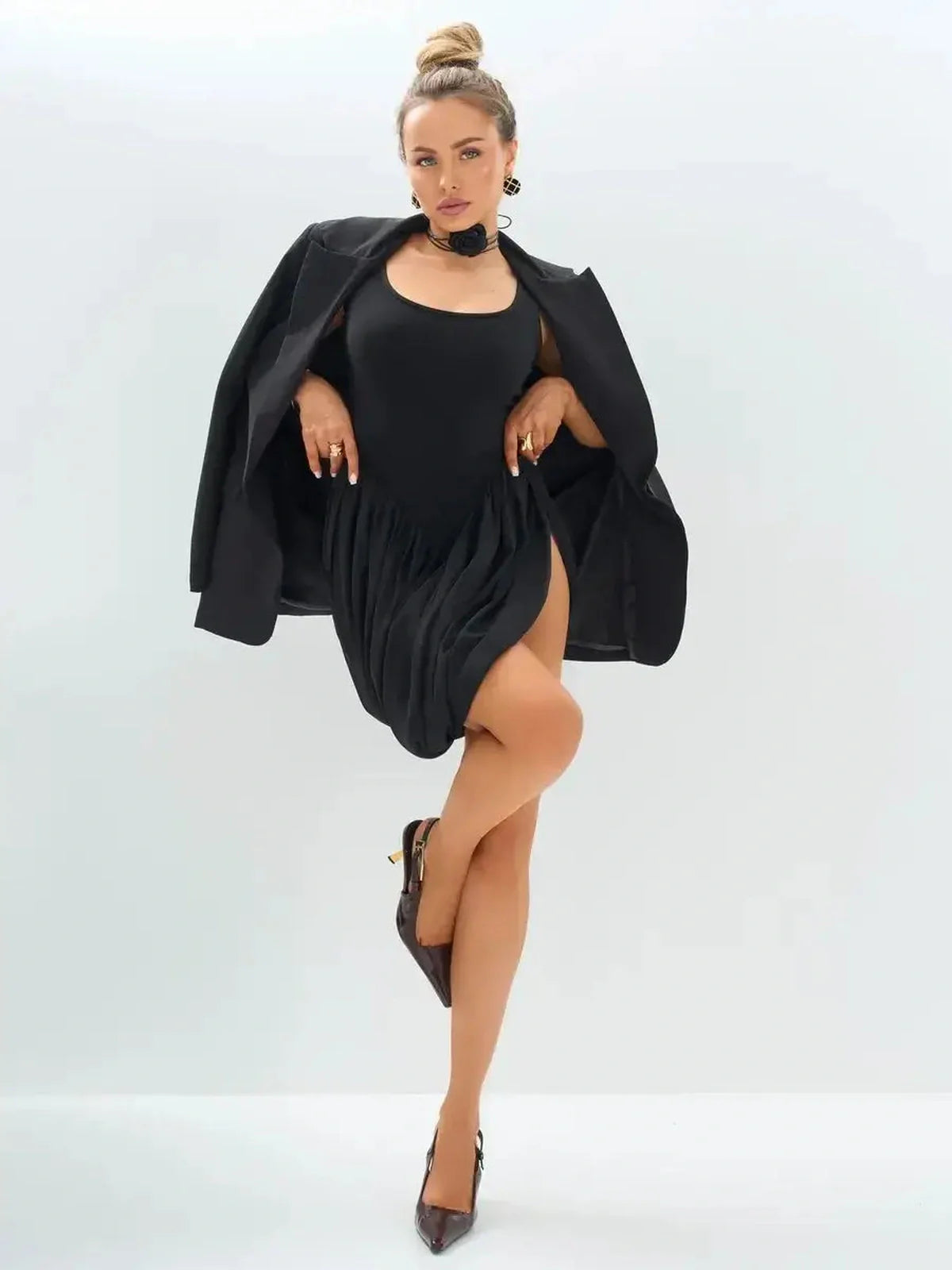 Model showcasing the Midnight Pulse black mini dress with delicate drapes, styled with a blazer and chic heels.