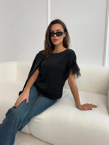 Elegant woman in Noiré Blouse with tulle ruffle detail, seated in a stylish setting, exuding modern femininity.