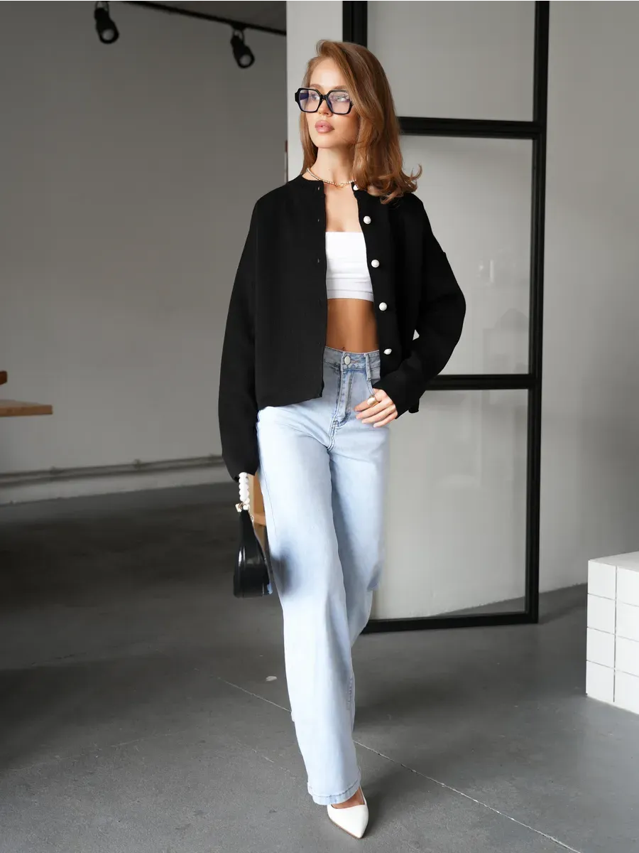 Model wearing Obsidian Cardigan by Lauven, stylish black knitwear paired with jeans and heels in a sophisticated setting.