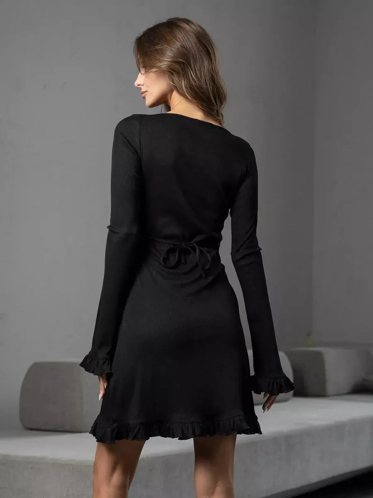 Model showcasing the back of the Noir Flare mini dress with lace-up detail and ruffled trim, emphasizing a sleek silhouette.
