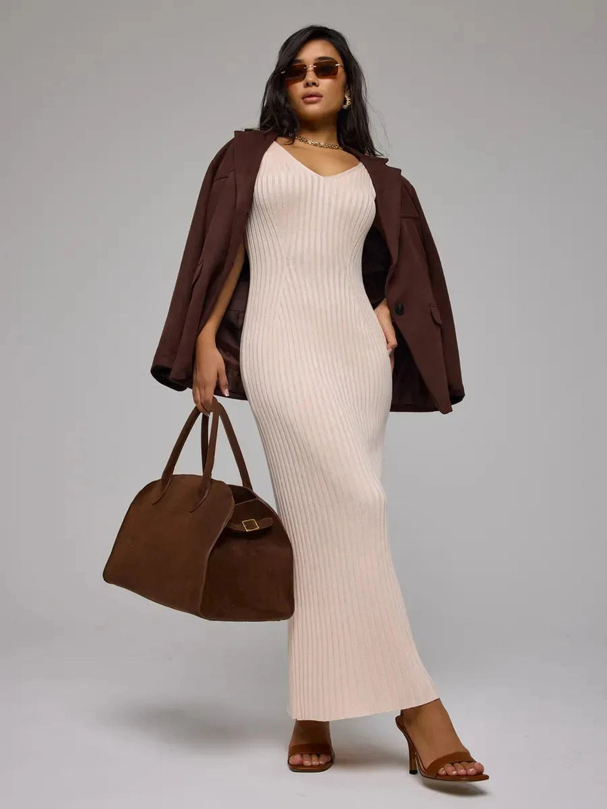 Model wearing the Rosette Maxi Dress by Lauven, a beige ribbed knit dress, styled with a brown jacket and handbag.