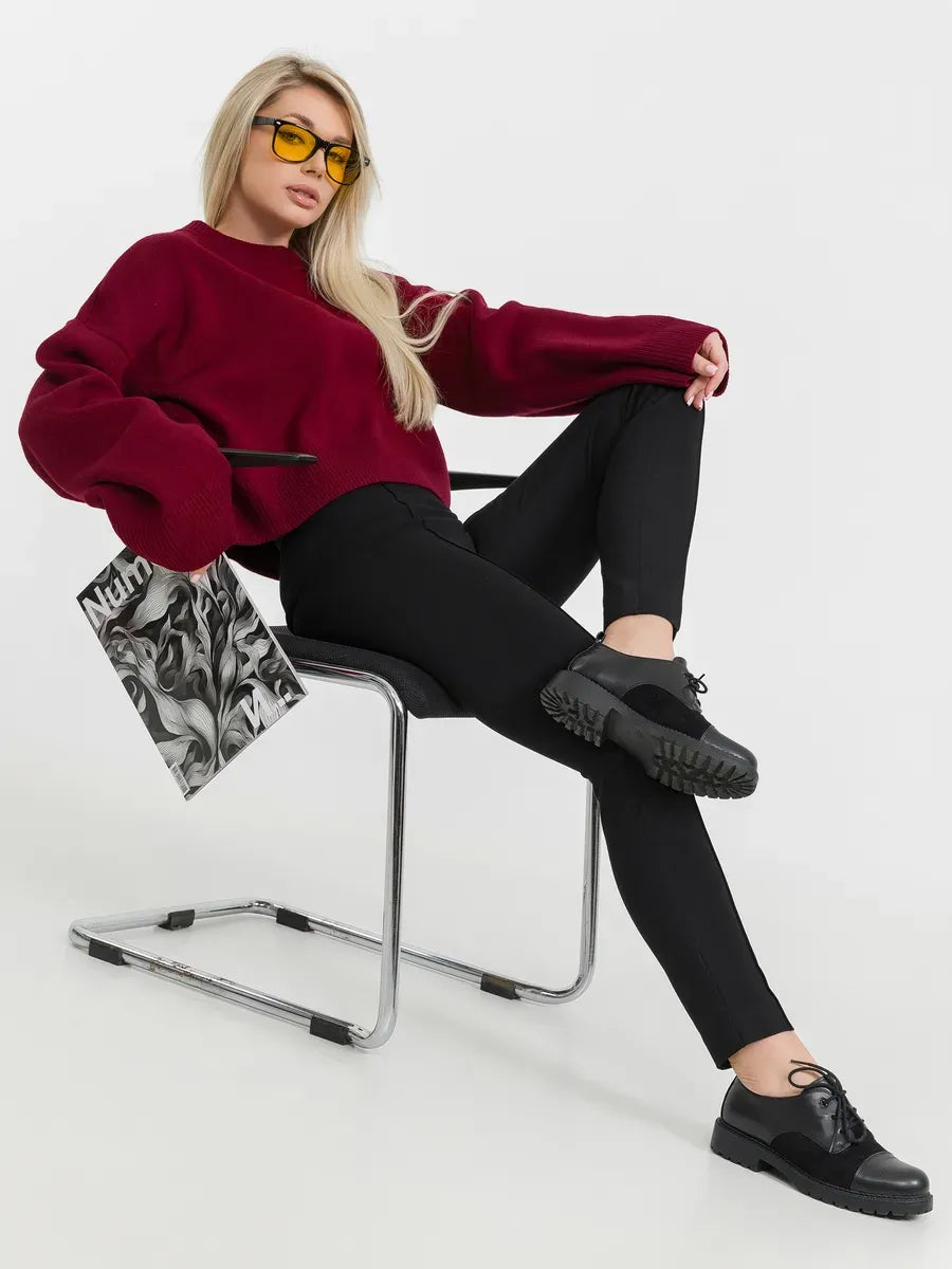 Model wearing Marbella Sweater in burgundy, showcasing modern minimalism, paired with sleek black pants.