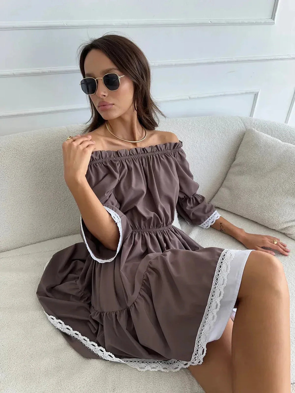 Woman in off-shoulder mocha brown mini dress with white ruffle trim, exuding summer charm and elegance.