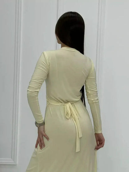 Back view of a woman wearing a Celeste Wrap Maxi Dress in buttercream, showcasing its sleek silhouette and elegant tie detail.