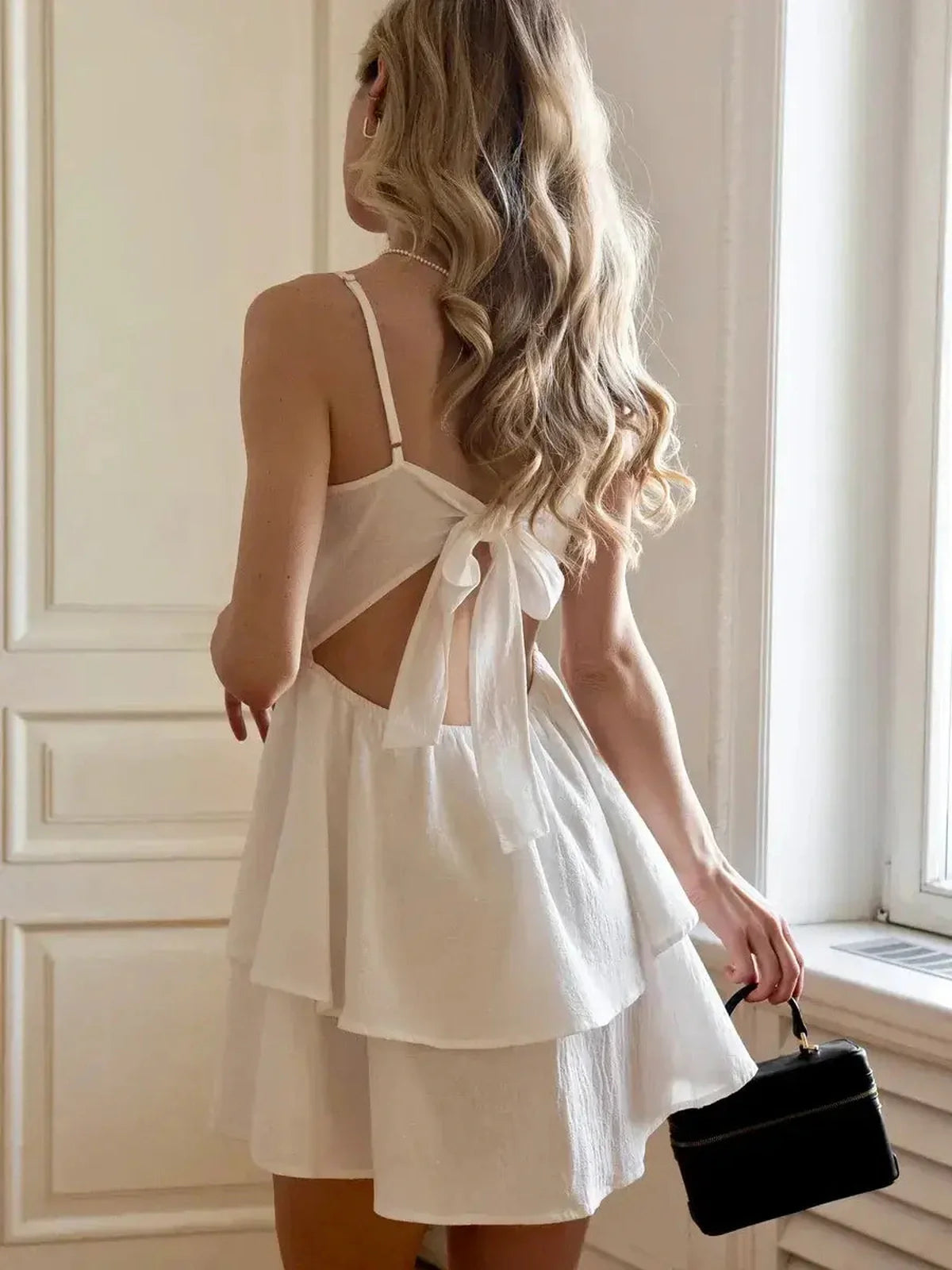Woman wearing a white Blanc Tier Mini Dress with a tiered skirt and back bow detail, styled for summer.
