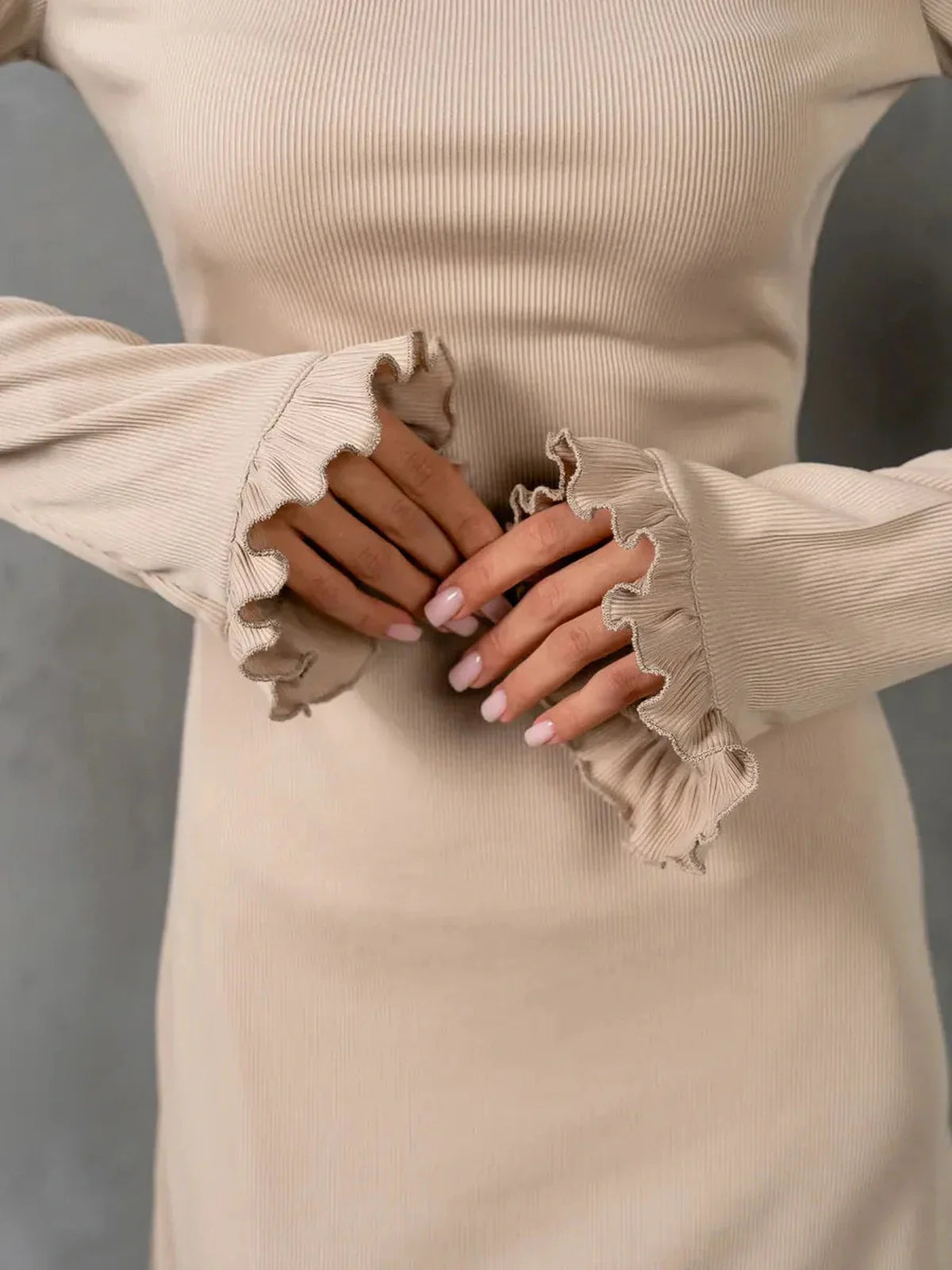 Close-up of elegant beige dress sleeves with ruffle accents, embodying modern minimalist style and soft femininity.