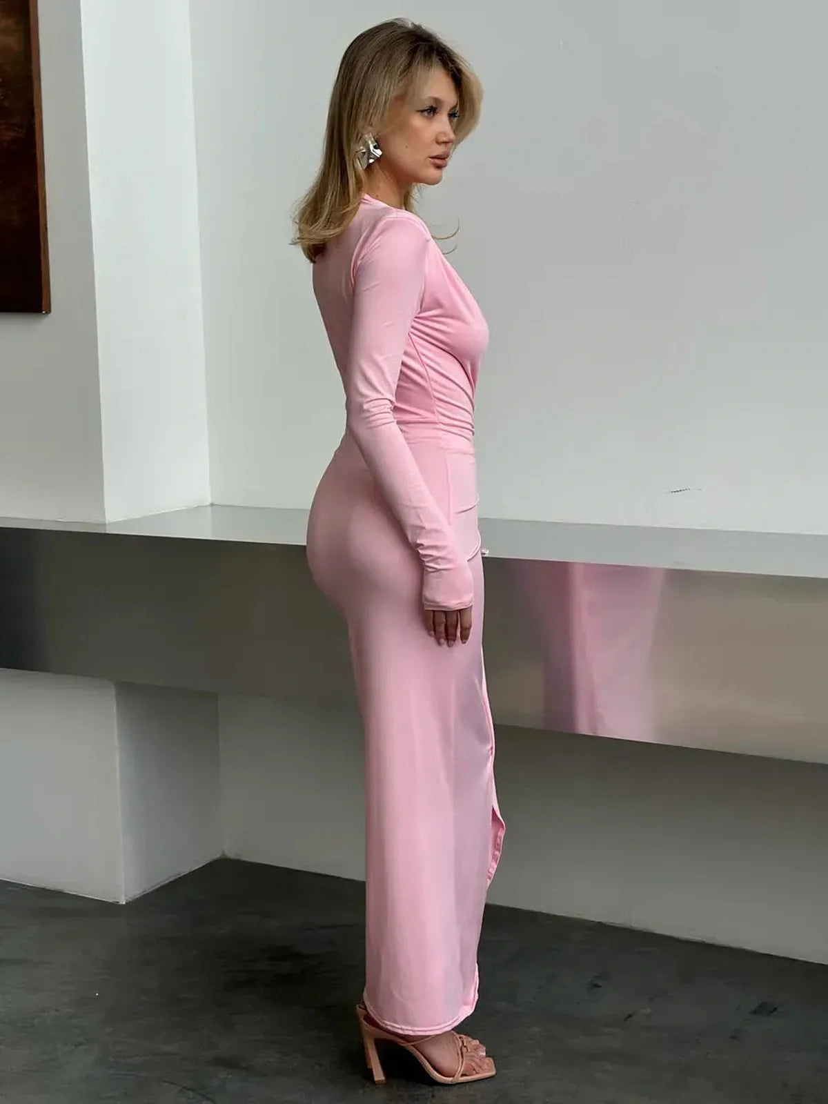 Model showcasing the Blush Muse Maxi Dress in soft pink, featuring long sleeves and a plunging neckline.