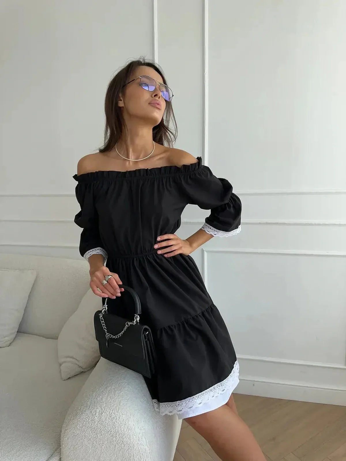 Woman in a black off-shoulder mini dress with white lace trim and tiered ruffles, showcasing a chic and romantic style.