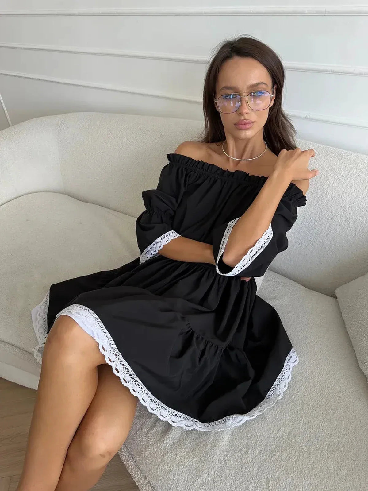Black mini dress with off-shoulder neckline and white lace trim, showcased in a relaxed fit.