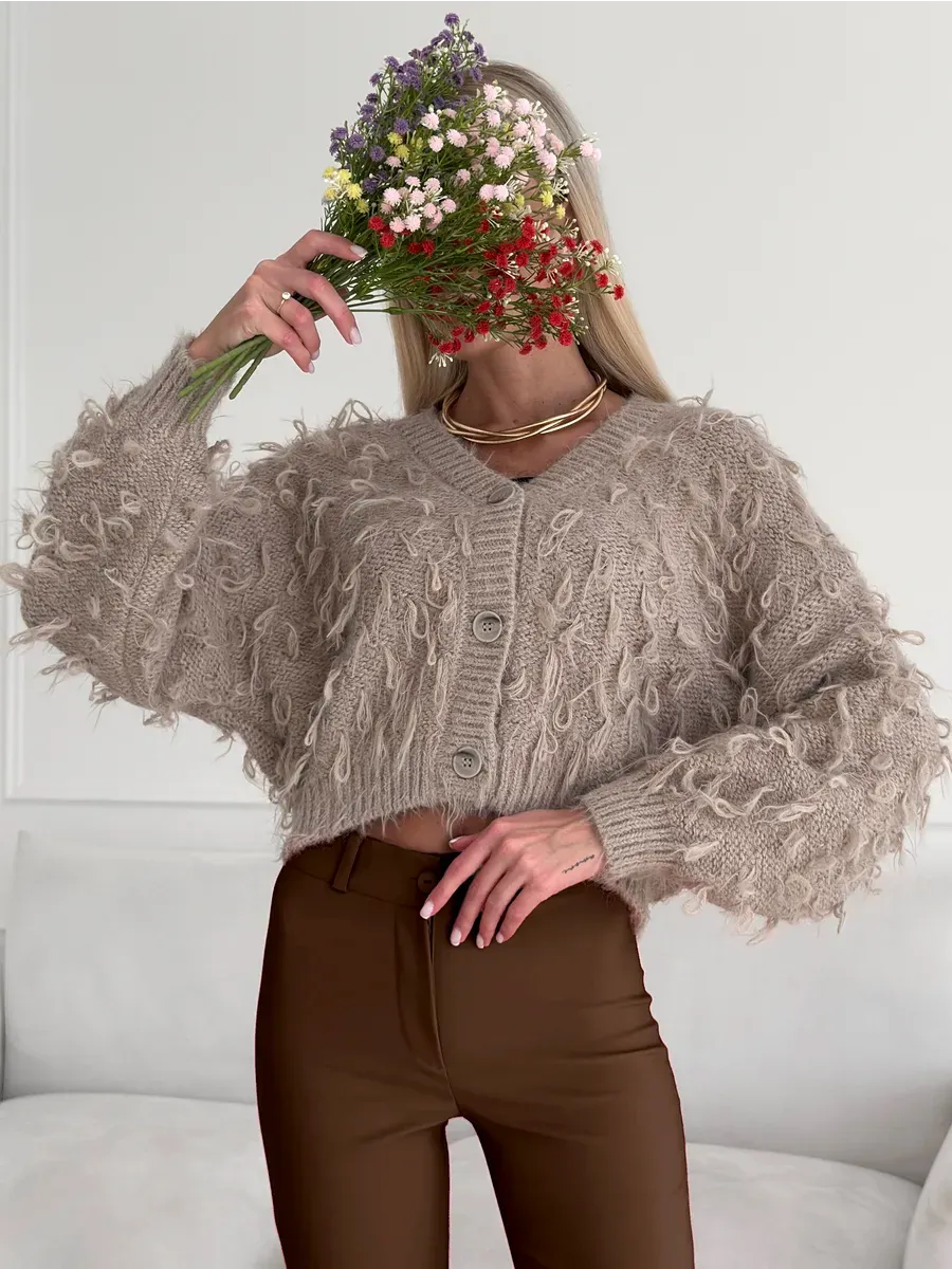 Sahara Cardigan by Lauven, cropped oversized beige bouclé knit with feathered fringe, styled with a bouquet of flowers.