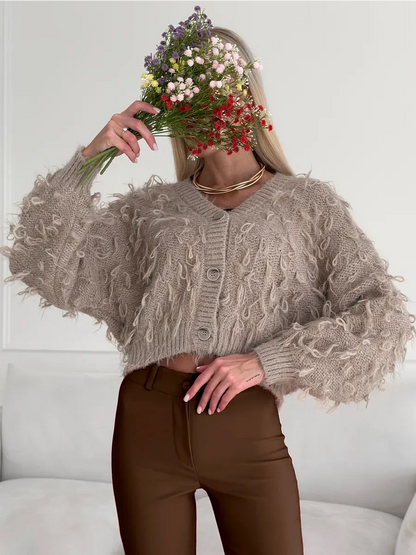 Sahara Cardigan by Lauven, cropped oversized beige bouclé knit with feathered fringe, styled with a bouquet of flowers.