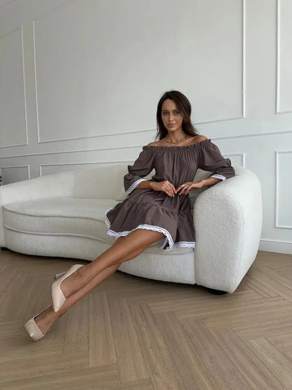 Chic model in mocha off-shoulder mini dress with white ruffle trim, styled elegantly on a modern white sofa.