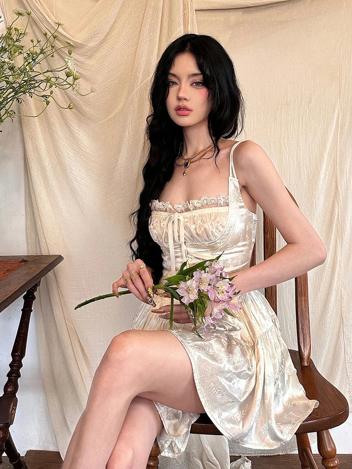 Model wearing the Ivy Mini Dress, a vintage-inspired white dress with lace detailing, holding flowers.