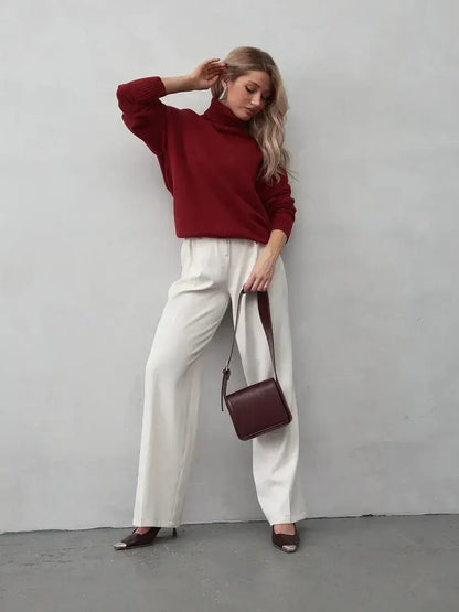 Model wearing Arden Sweater by Lauven, a burgundy turtleneck, paired with white pants and burgundy handbag.