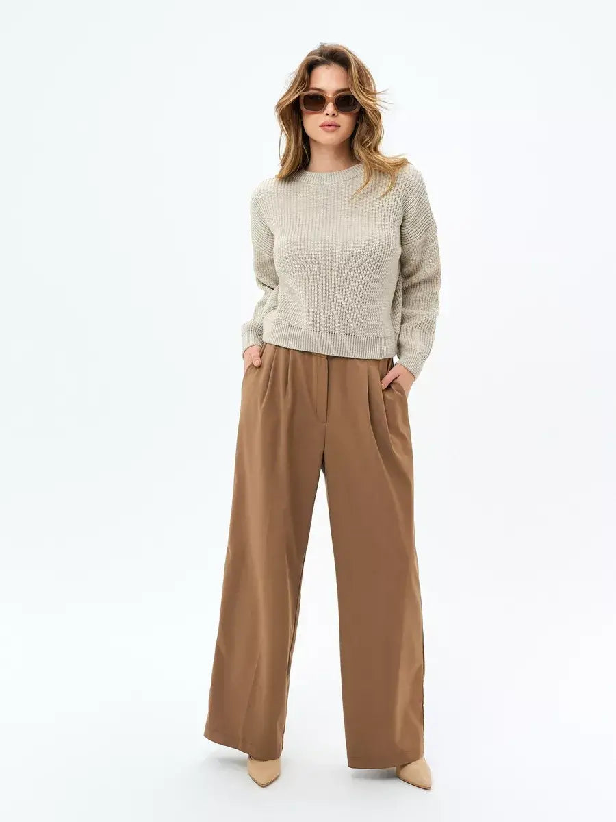 A woman wearing an oversized light beige Astra Sweater by Lauven, paired with wide-leg brown pants and sunglasses.