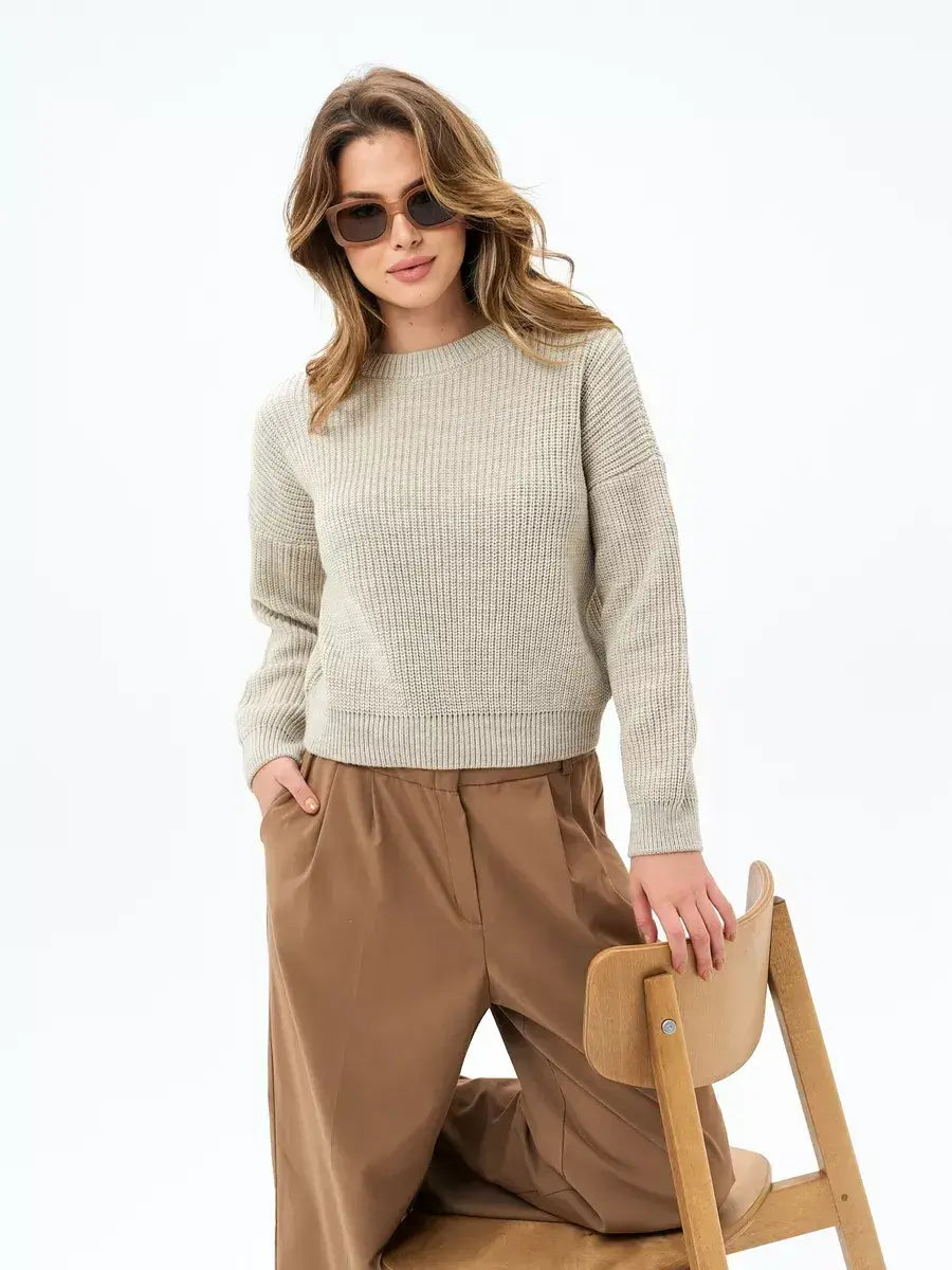 A stylish woman wearing the Lauven Astra Sweater in light beige, paired with relaxed pants, exuding chic comfort.