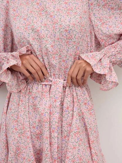 Close-up of Lauven Blush Bloom Mini Dress in soft pink floral print, showcasing elasticated waist and flared skirt with ruffles.