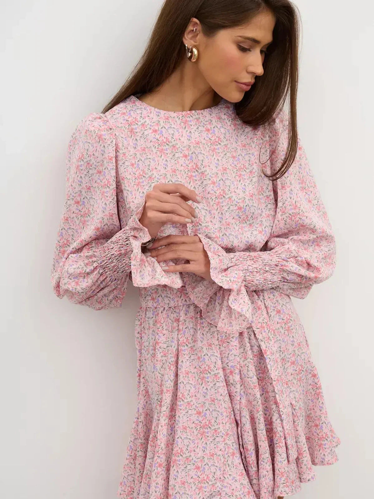 Lauven Blush Bloom Mini Dress featuring soft pink floral print, round neck, long sleeves, and flared skirt with ruffles.