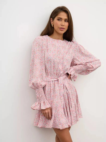 Model wearing Lauven Blush Bloom Mini Dress, soft pink floral, round neck, long sleeves, and flared skirt.