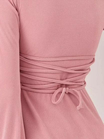 Back view of the Blush Flare mini dress by Lauven, showcasing the soft pink ribbed fabric and stylish tie detail.