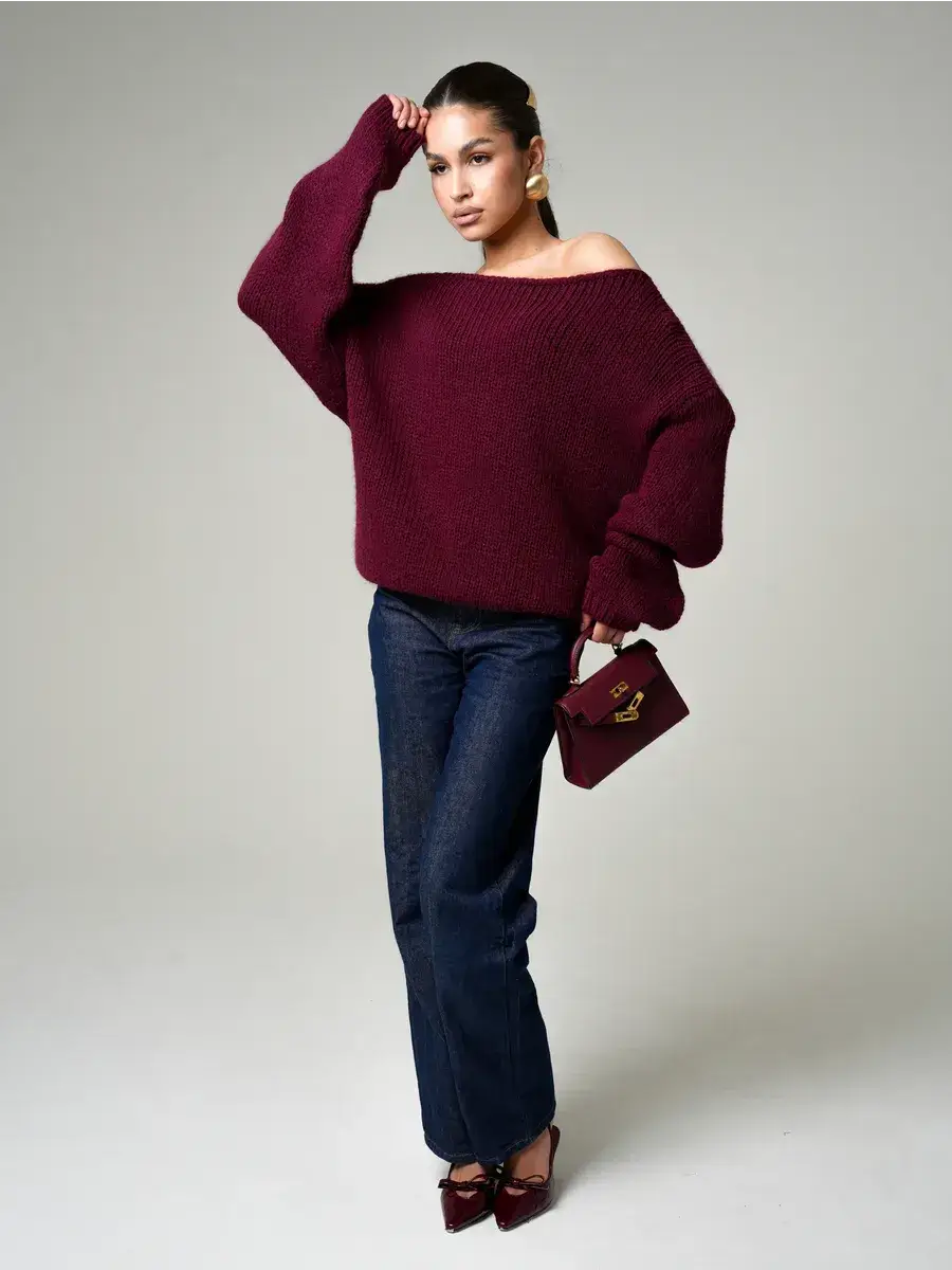 Model showcasing the Bordeaux Sweater by Lauven, an oversized off-shoulder knit in deep wine, paired with denim.