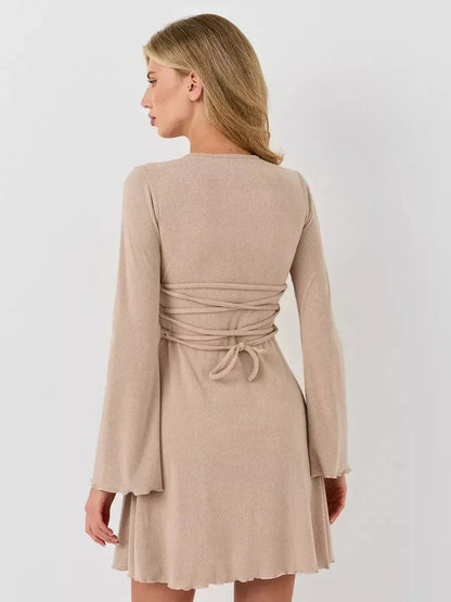 Back view of a woman in a warm beige Café Ribbon mini dress by Lauven with long bell sleeves and a tied waist.