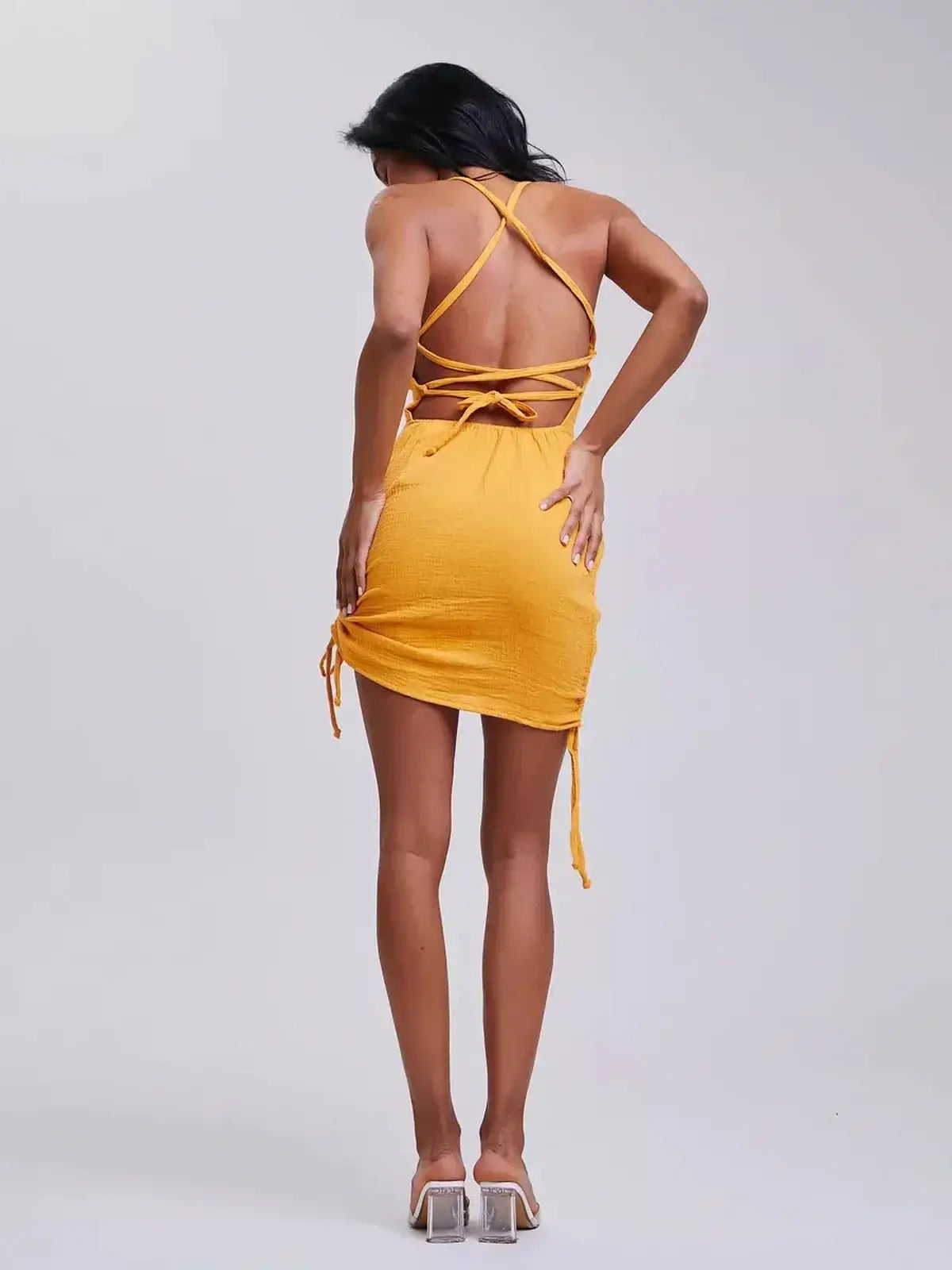Back view of a model in a yellow mini dress with crisscross straps, showcasing Lauven's Citrus Rush design.