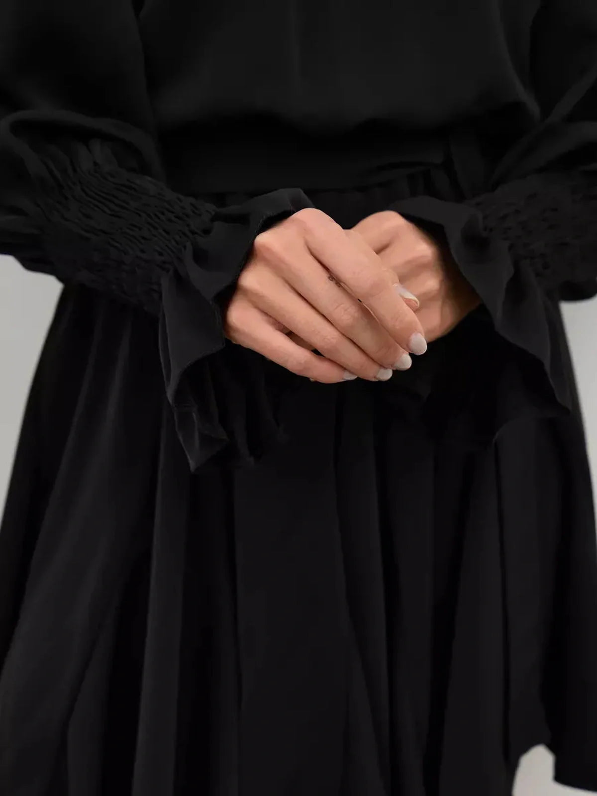 Close-up of hands elegantly clasped, showcasing the ruffled sleeves of the Lauven Eclipse Mini Dress in black.
