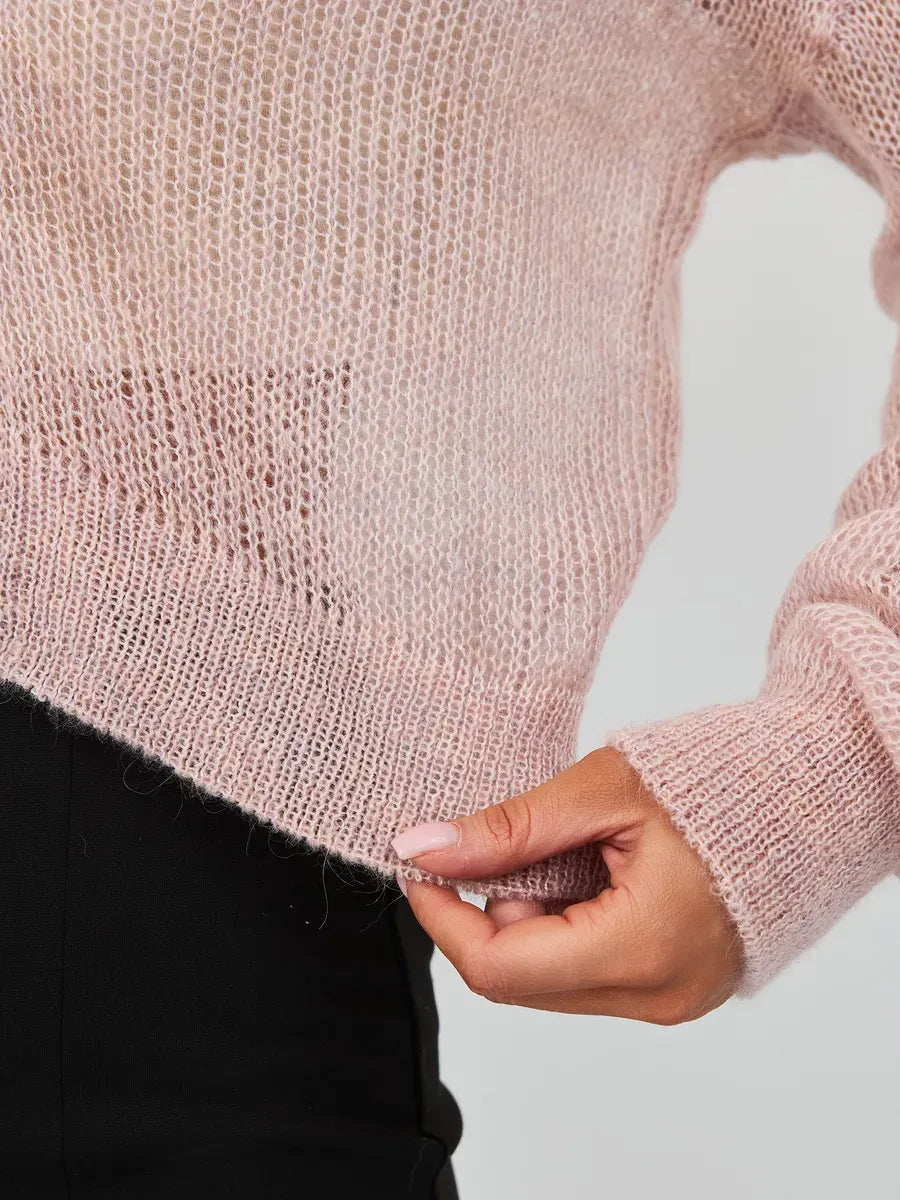 Close-up of a woman's hand holding the hem of the Rose Cardigan by Lauven, showcasing lightweight pink mohair-blend knitwear.