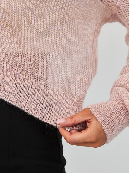 Close-up of a woman's hand holding the hem of the Rose Cardigan by Lauven, showcasing lightweight pink mohair-blend knitwear.