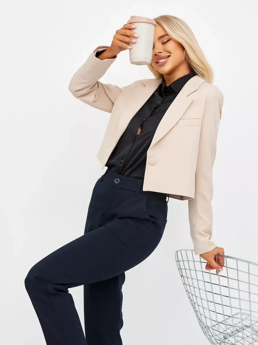 Woman wearing a Sandstone Blazer by Lauven, enjoying coffee, styled with black shirt and navy pants.