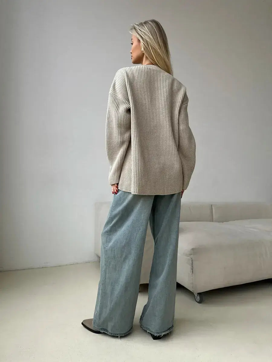 A woman wearing a relaxed oversized beige knit Sierra Sweater by Lauven, styled with wide-leg jeans.