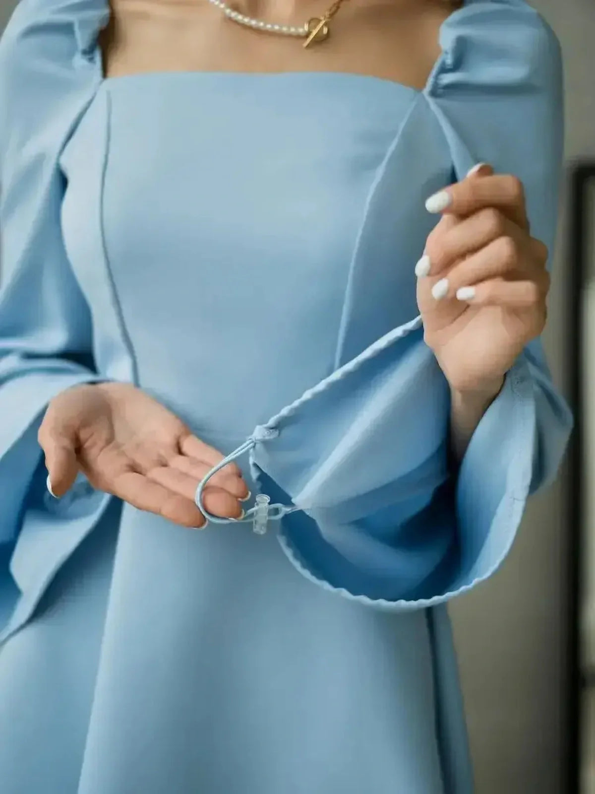 Light blue mini dress with elegant puff sleeves and a square neckline, showcasing a woman's hand holding a strap.