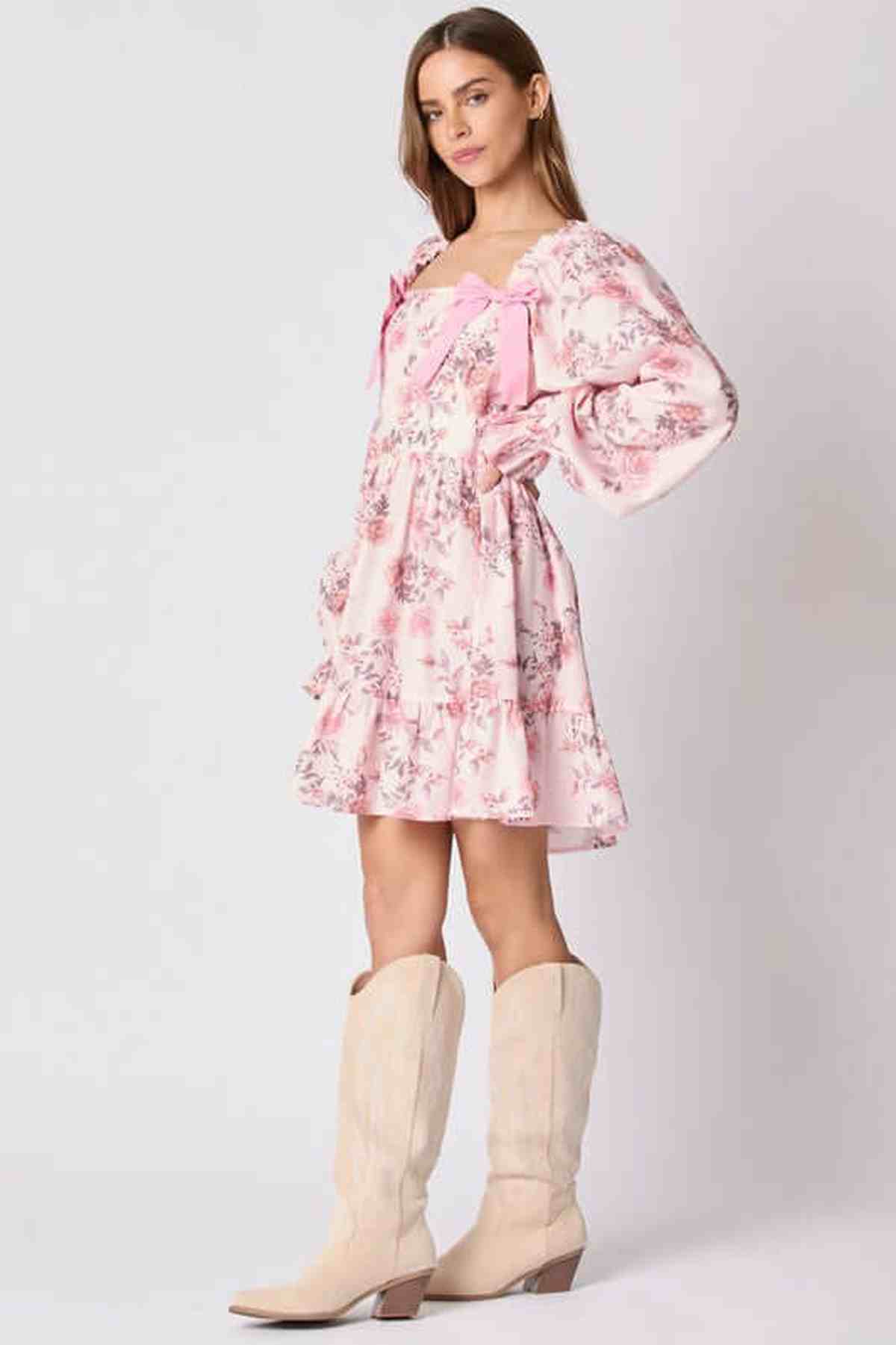 Model wearing the Lila Mini Dress, a floral pink dress with bow accents, paired with stylish knee-high boots.