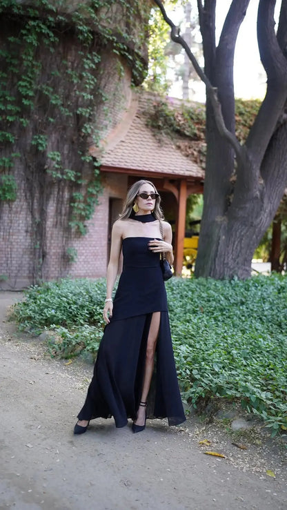 Elegant woman in a strapless black maxi dress with a thigh-high slit, perfect for cocktail events or formal occasions.