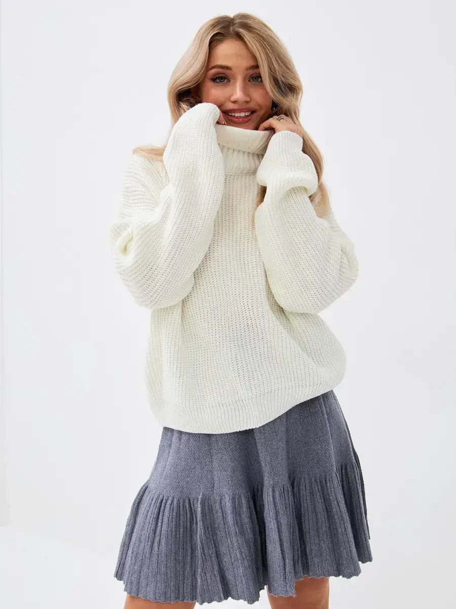 Model wearing the Lyra Sweater by Lauven, an oversized ivory knit with high neck paired with a grey flared skirt.