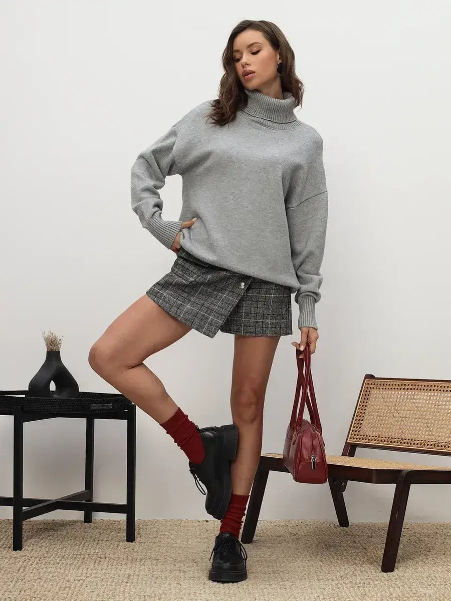 Lyra Sweater by Lauven, light grey turtleneck knitwear styled with a plaid skirt and red accessories.
