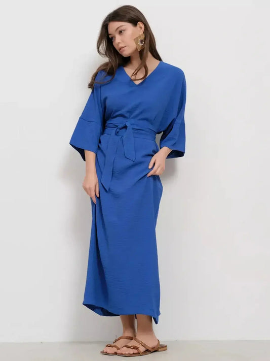 Model wearing a deep V-neck, relaxed-fit blue maxi dress with tie-belt, exuding modern elegance.