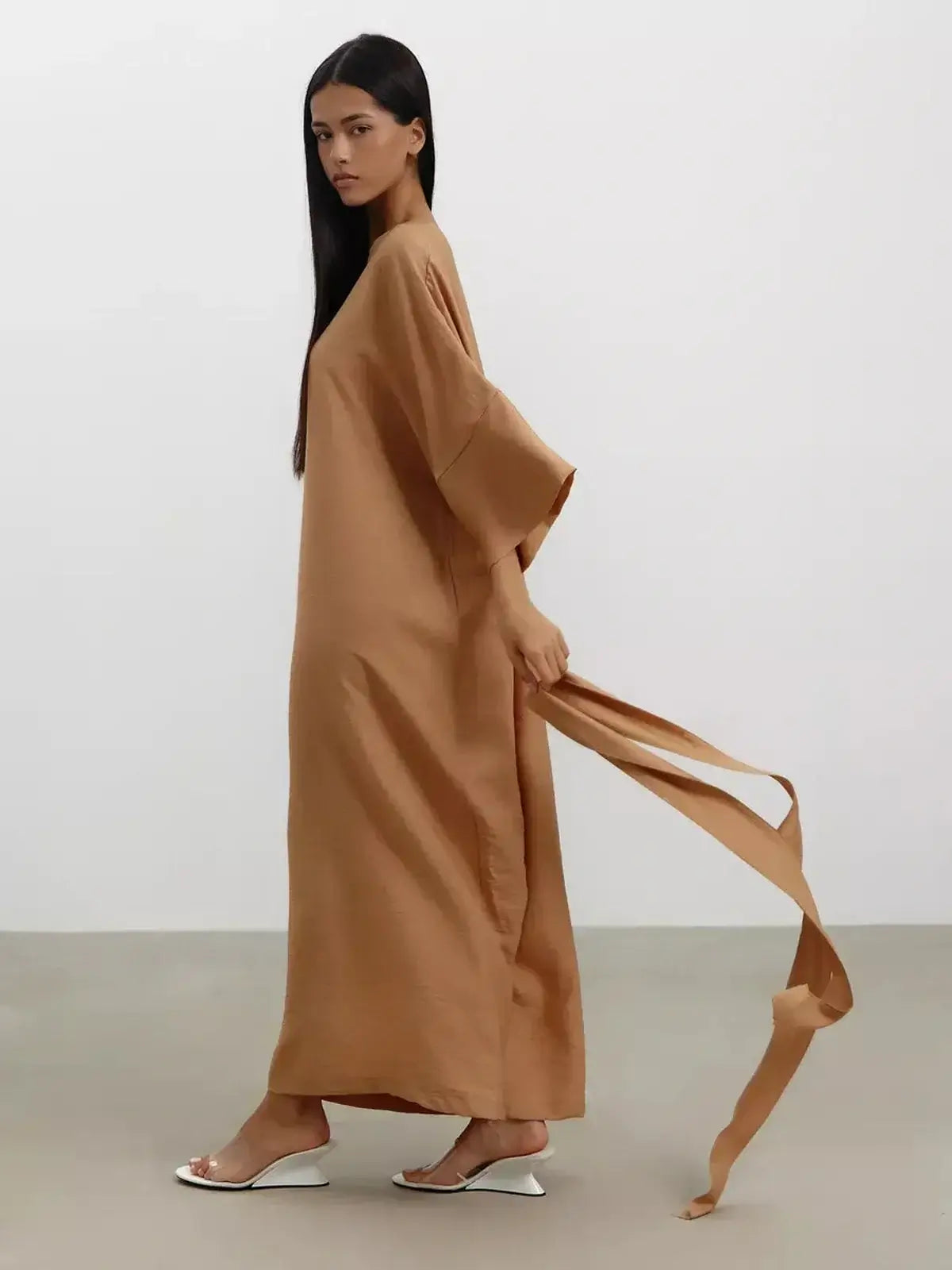Model wearing a flowing maxi dress in sandstone hue, featuring wide kimono sleeves and a detachable tie belt.