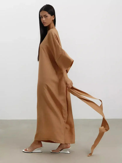 Model wearing a flowing maxi dress in sandstone hue, featuring wide kimono sleeves and a detachable tie belt.