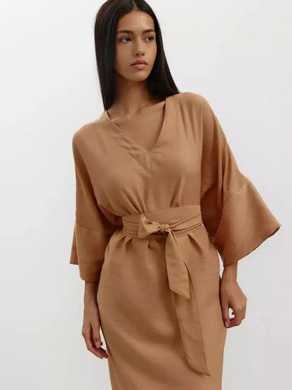 Model wearing the Maxi Dress Dune Whisper in a sandstone hue featuring wide sleeves and a tied waist.