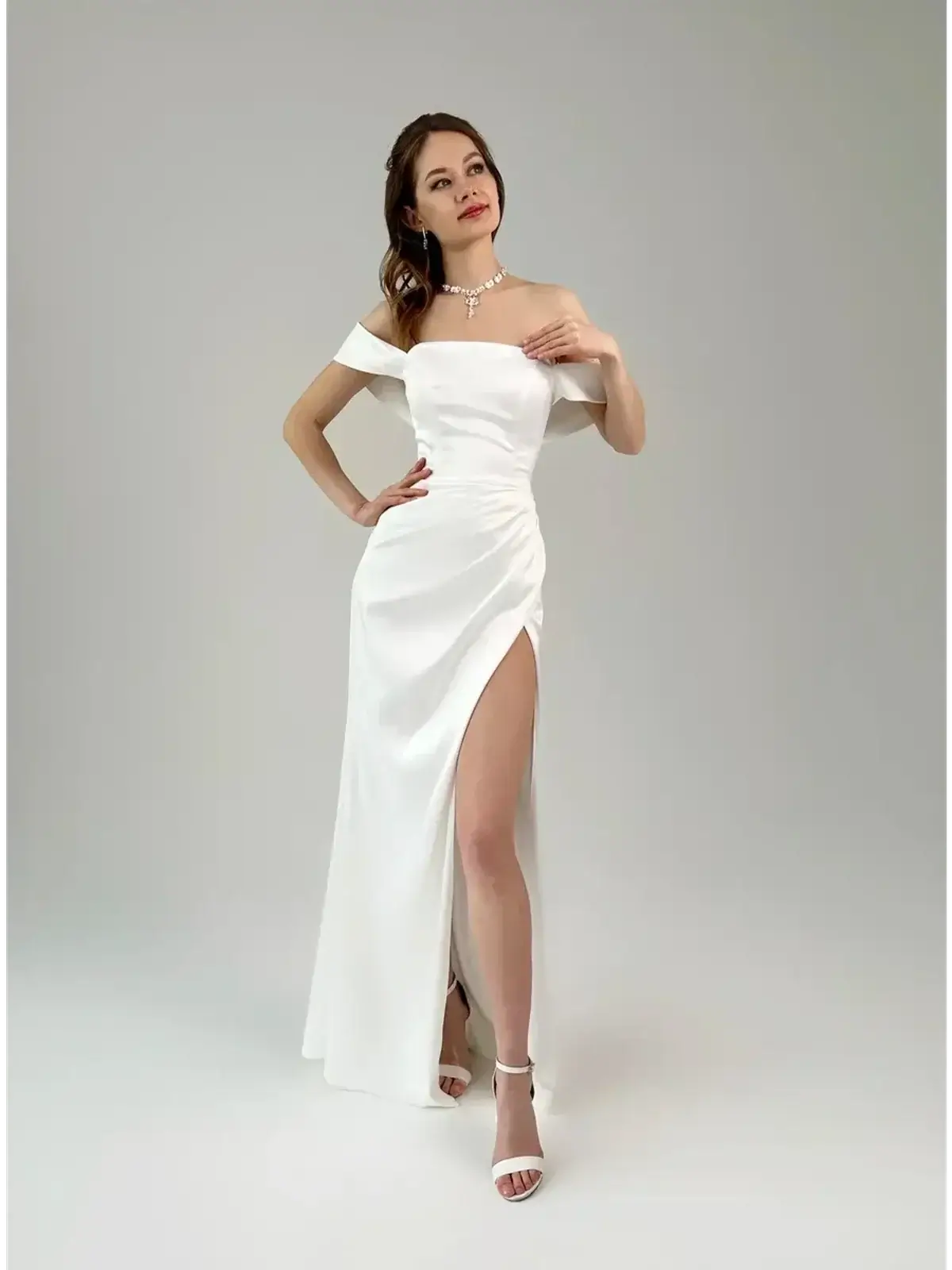 Model in a white satin maxi dress with off-shoulder neckline and thigh-high slit, exuding elegance and glamour.