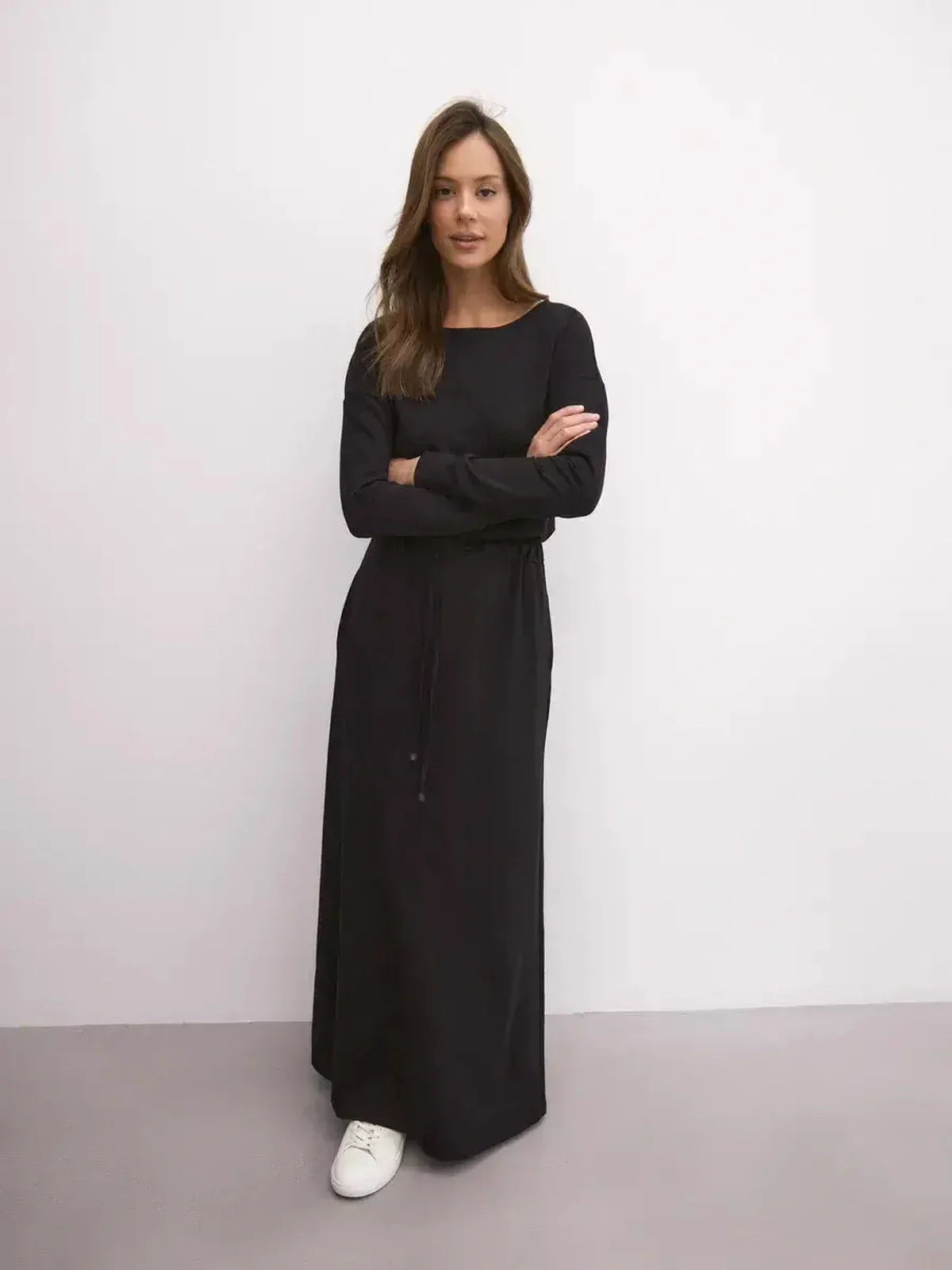 Model wearing a black maxi dress with long sleeves and drawstring waist, showcasing urban elegance and relaxed fit.