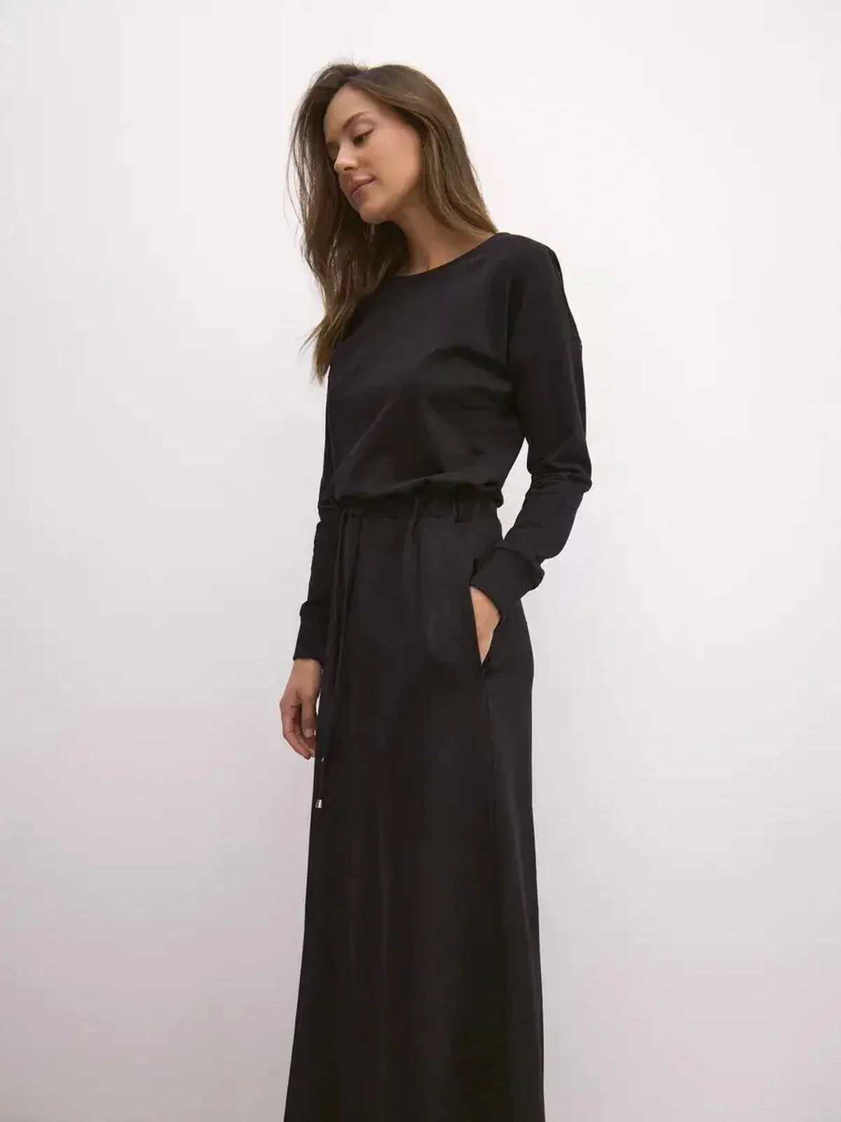 Model wearing a black maxi dress with long sleeves and cinched waist, showcasing urban elegance and comfort.