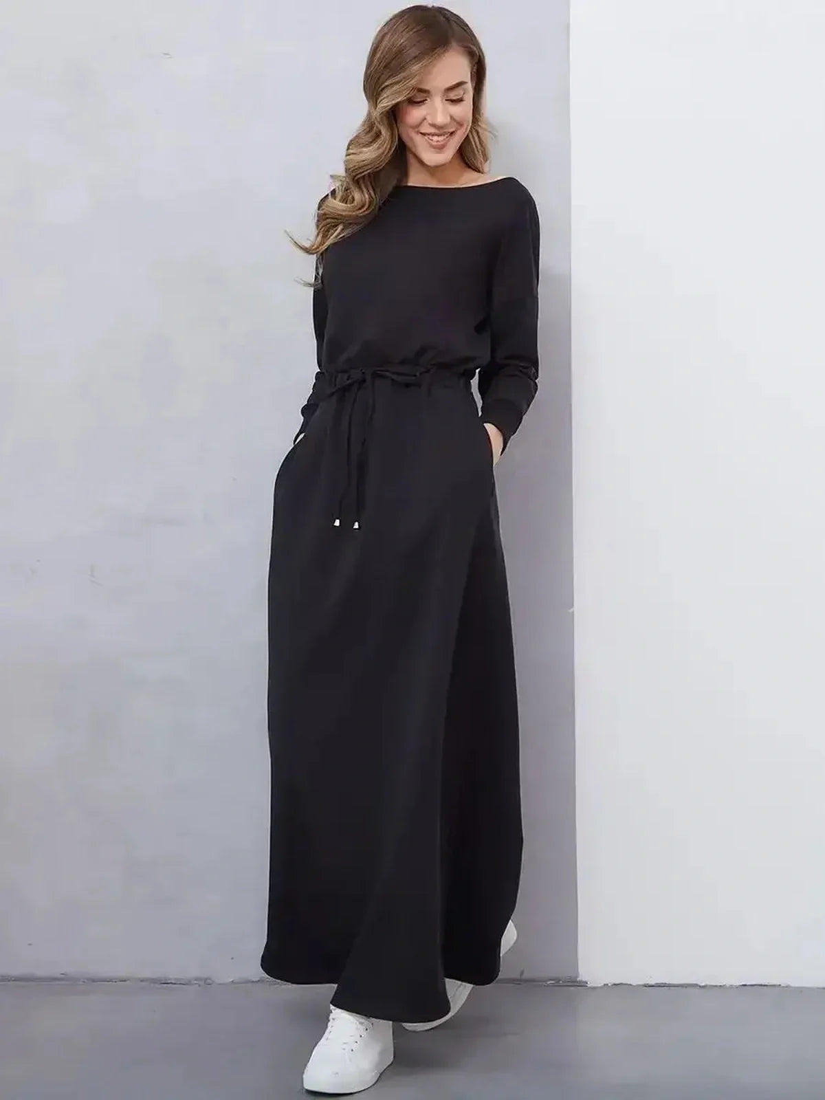 Woman in a sleek black maxi dress with a cinched waist and long sleeves, showcasing urban elegance and comfort.