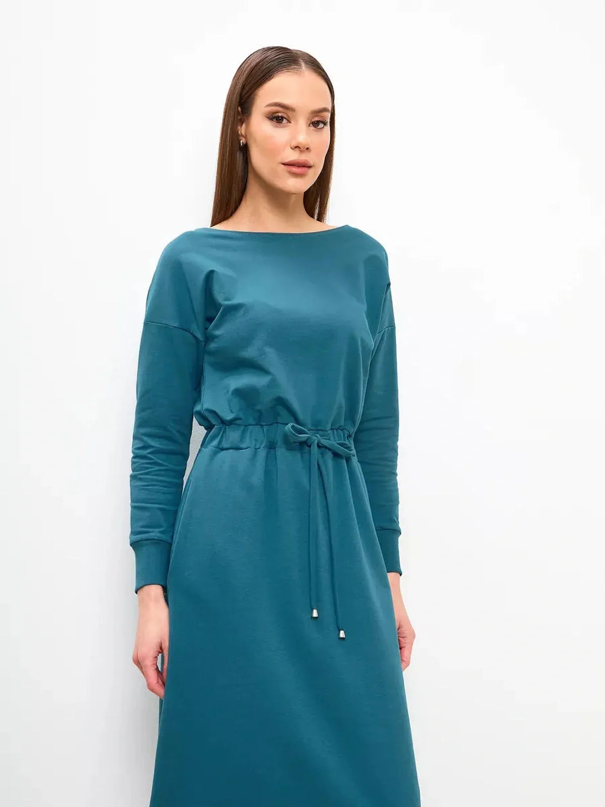Model wearing a teal maxi dress with a cinched waist and long sleeves, showcasing modern elegance and comfort.