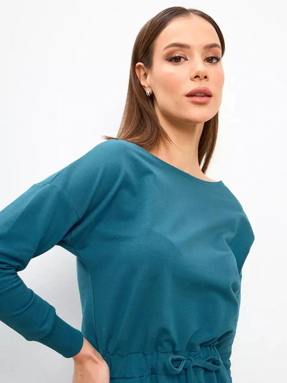 Model showcasing a stylish teal maxi dress with an elegant neckline and cinched waist.