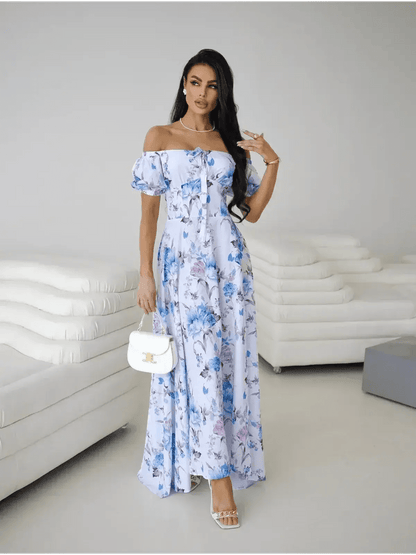 Model wearing an off-shoulder white and blue floral maxi dress with puff sleeves and thigh-high slit.