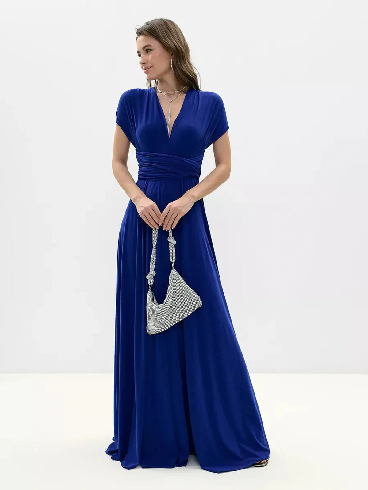 Elegant woman in a vibrant blue maxi dress with a twisted back, holding a stylish grey bag.